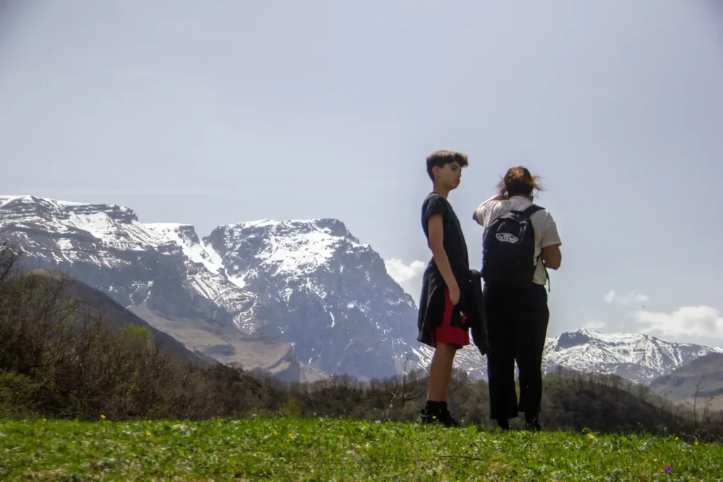 Two hikers looking towards snow-capped peaks above the valley near Laza