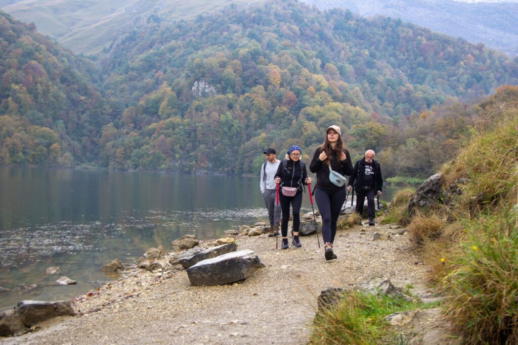 Hikers on a lakeside trail below autumn-colored forest in Azerbaijan
