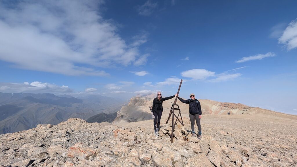 Two hikers at the summit marker on the rocky Gizilgaya plateau under a blue sky