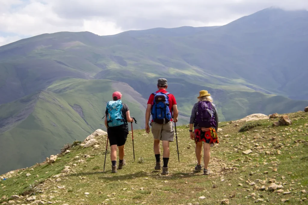 Three hikers walking along a grassy ridge toward the mountains of the Greater Caucasus