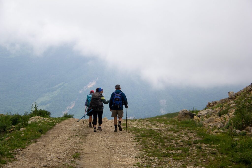 Hikers walking along a dirt track towards low clouds in the mountains