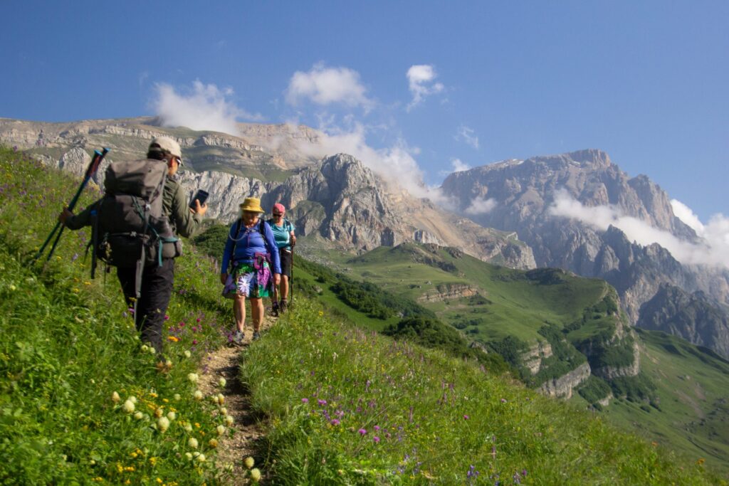 Hikers on a trail through a wildflower meadow below the Shahdag cliffs