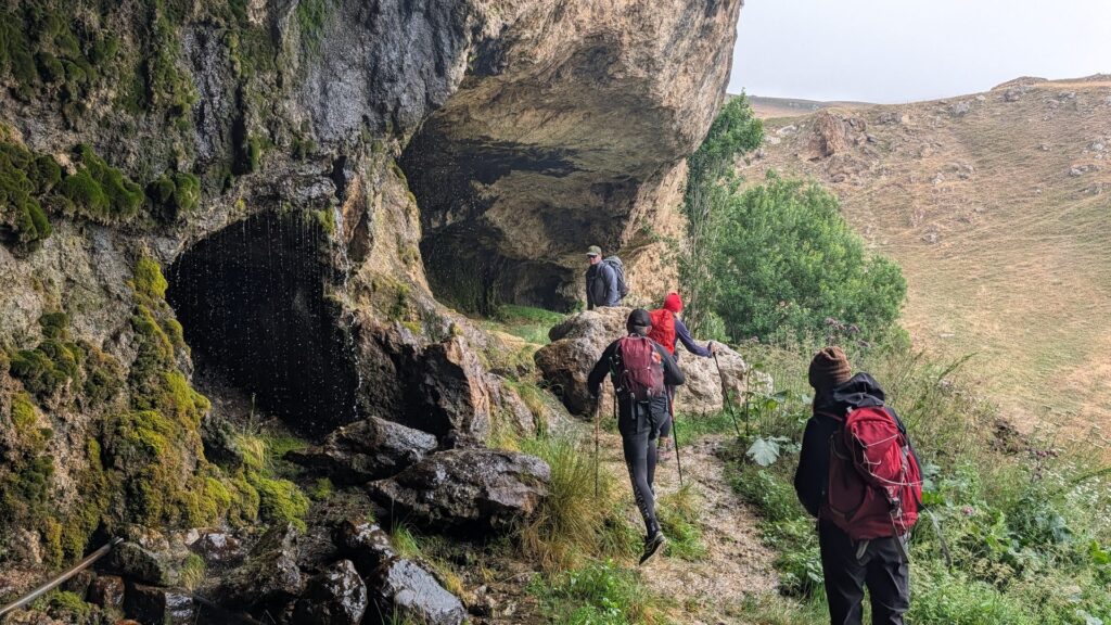 Hikers on the trail to a small waterfall hidden in a cave near Khinalig