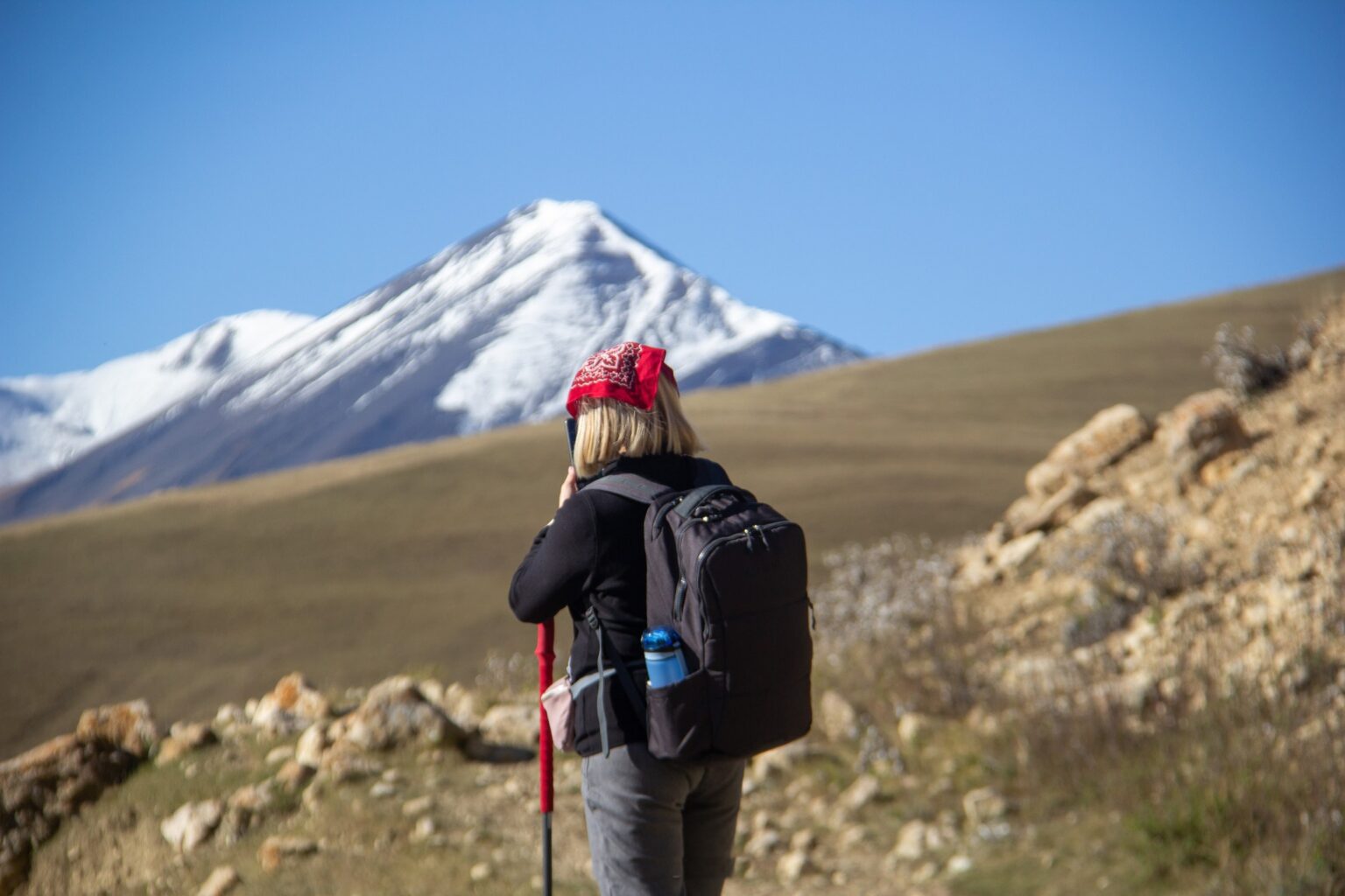 Hiker on a golden autumn trail near Khinalig, looking towards a snow-capped Caucasus peak