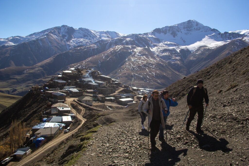 Small group of hikers on a trail above Khinalig village in autumn, with snow-capped Caucasus peaks behind