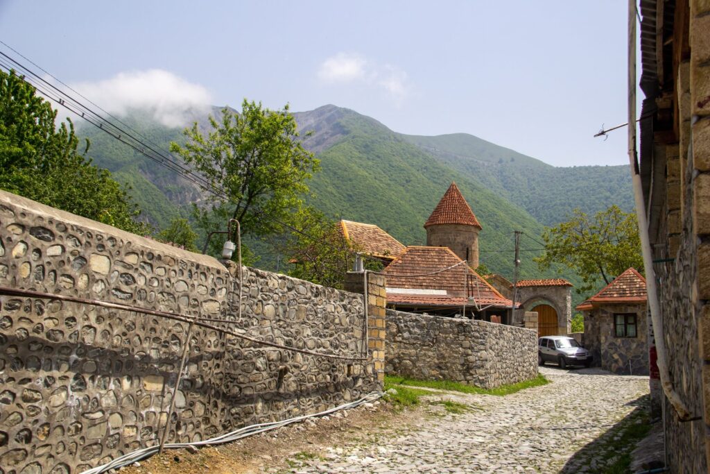 Stone walls and the red-roofed old church in Kish village near Sheki, with green mountains behind